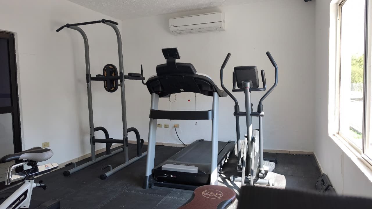 Un gimnasio con equipamiento de ejercicio, incluyendo una caminadora, elíptica y máquinas de pesas.