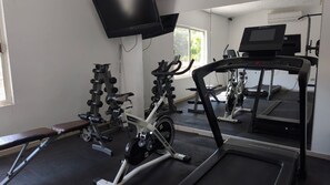 Ett gym med träningsutrustning, inklusive löpband, styrketräningsmaskiner och en träningsbänk.