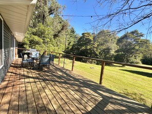 Une terrasse en bois avec des meubles d’extérieur, un barbecue et une vue sur une pelouse verdoyante bordée d’arbres.