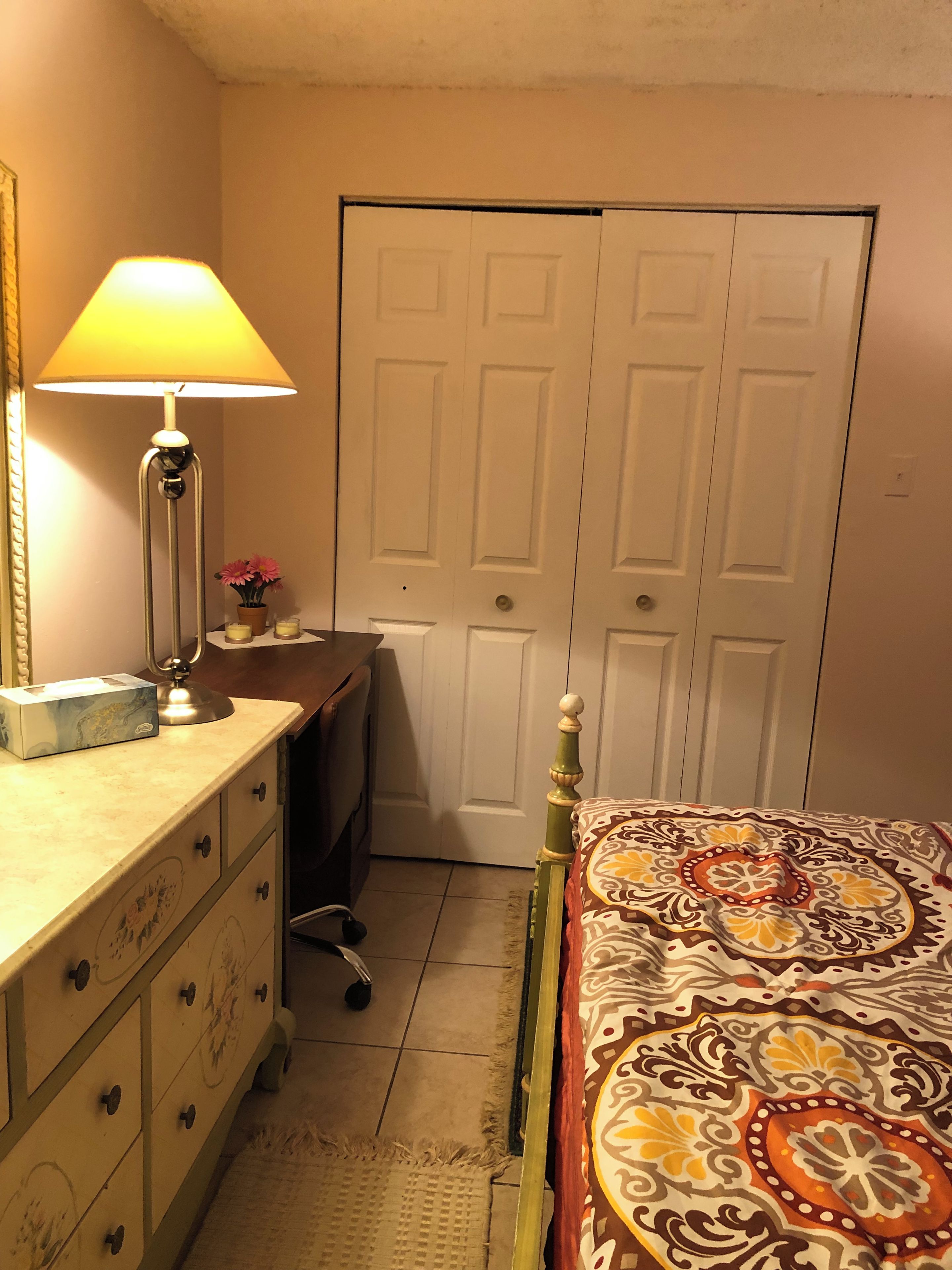 Un dormitorio con cama, cómoda, escritorio, lámpara y una puerta cerrada.