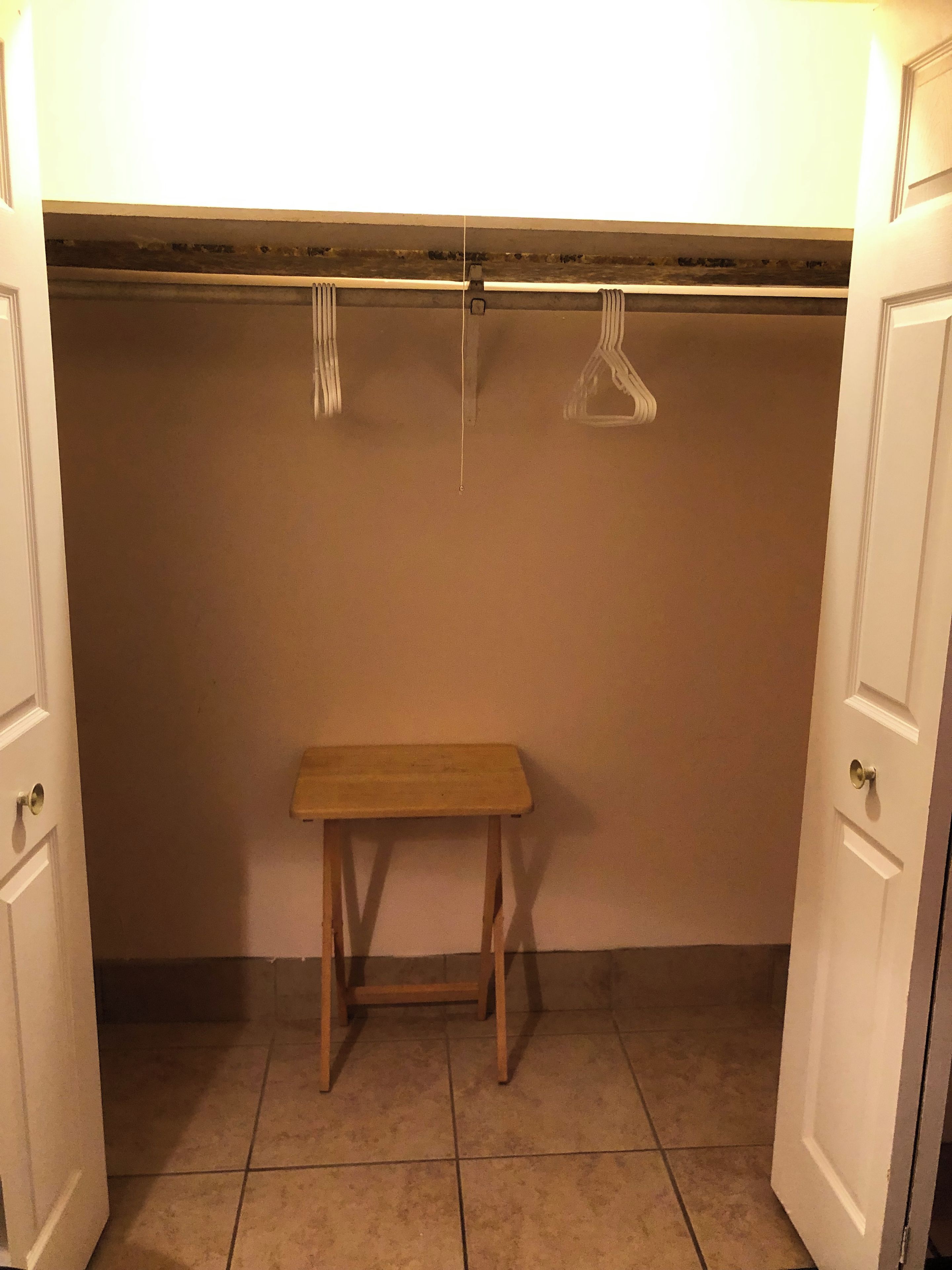 Un pequeño banco de madera en un armario con una barra para colgar encima.