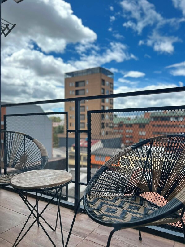 A balcony with two chairs and a table, a metal railing, and a view of a building in the background. - New Listing (Bogotá)