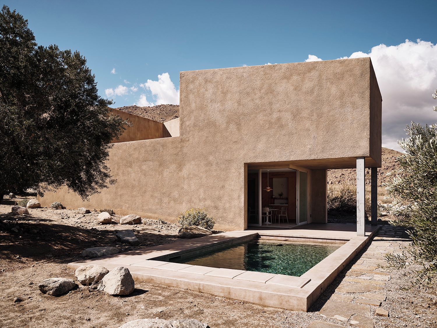 A modern building with a pool, surrounded by rocks and sparse vegetation.