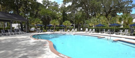 A swimming pool with lounge chairs and umbrellas, surrounded by trees.