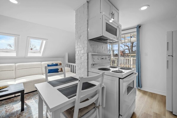 Eine moderne Küche mit weißen Geräten, ein Essbereich mit weißem Tisch und Stühlen und ein Ausblick durch ein Fenster.