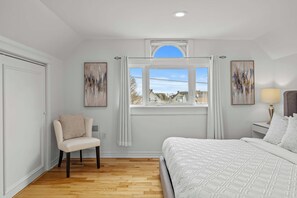 Ein Schlafzimmer mit einem Bett, einem Sessel, einem Fenster mit Vorhängen und zwei Wandbildern.