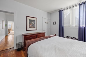 Ein Schlafzimmer mit einem Bett, einem Schminktisch, einer Tür und einem Fenster mit Vorhängen.