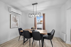 Een eethoek met een houten tafel, zwarte stoelen, een hanglamp en uitzicht op buiten.