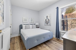 Een slaapkamer met een bed, een radiator, een raam met gordijnen en kunstwerken aan de wanden.