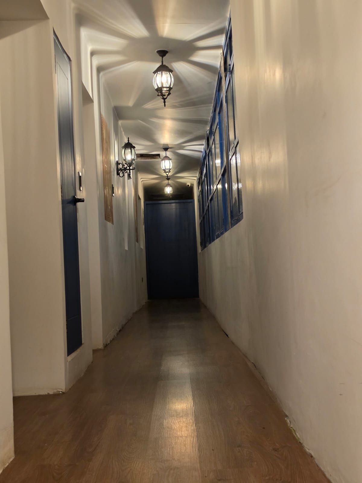 Un couloir avec un plancher en bois, des murs blancs et une porte bleue au fond.