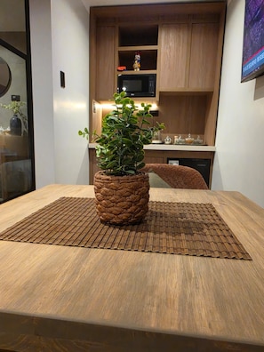 A dining table with a woven placemat, a potted plant, and a wooden cabinet in the background. - New Listing (Cusco)