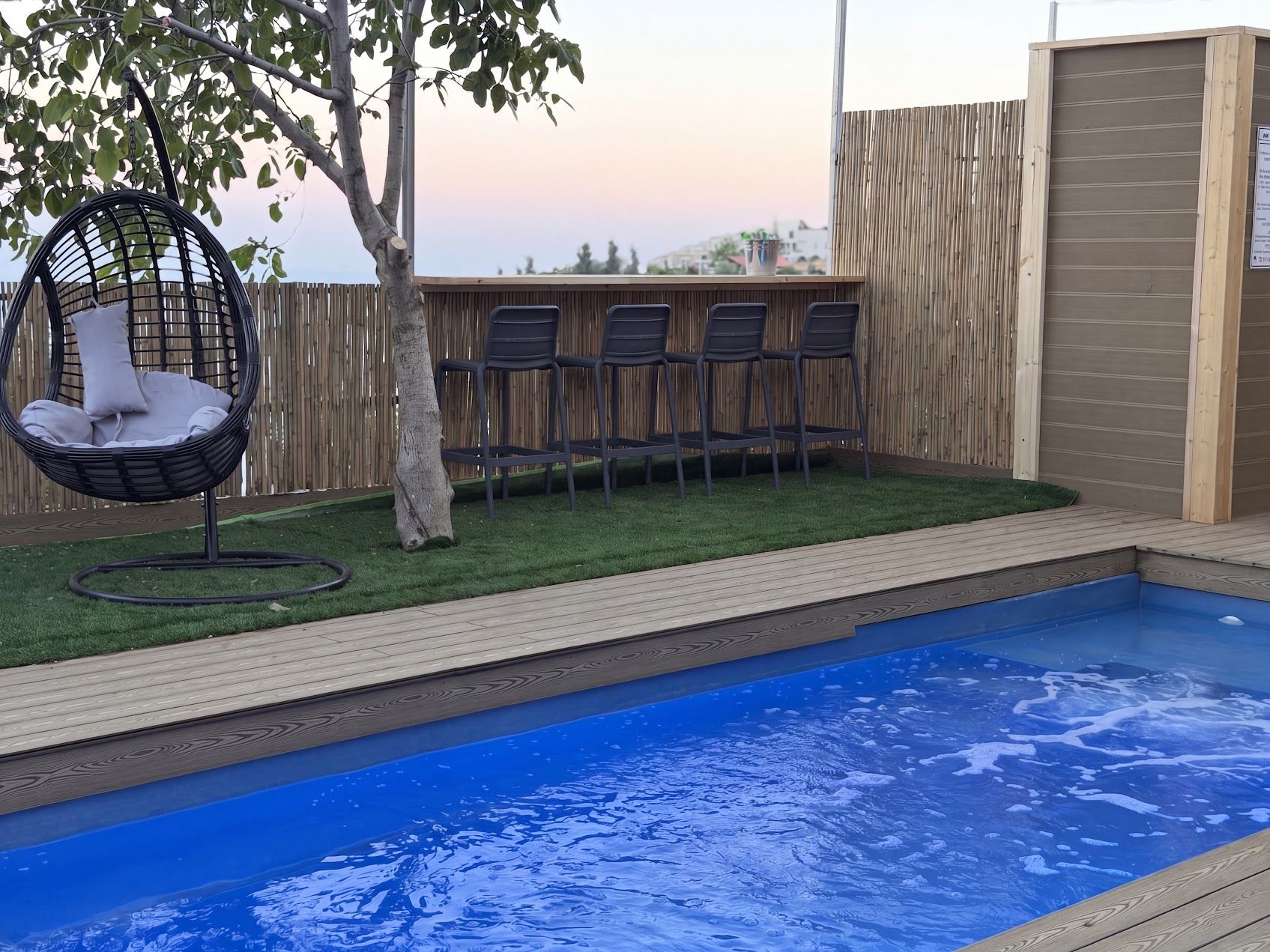 A swimming pool with a wooden deck, a hanging chair, and a row of chairs.