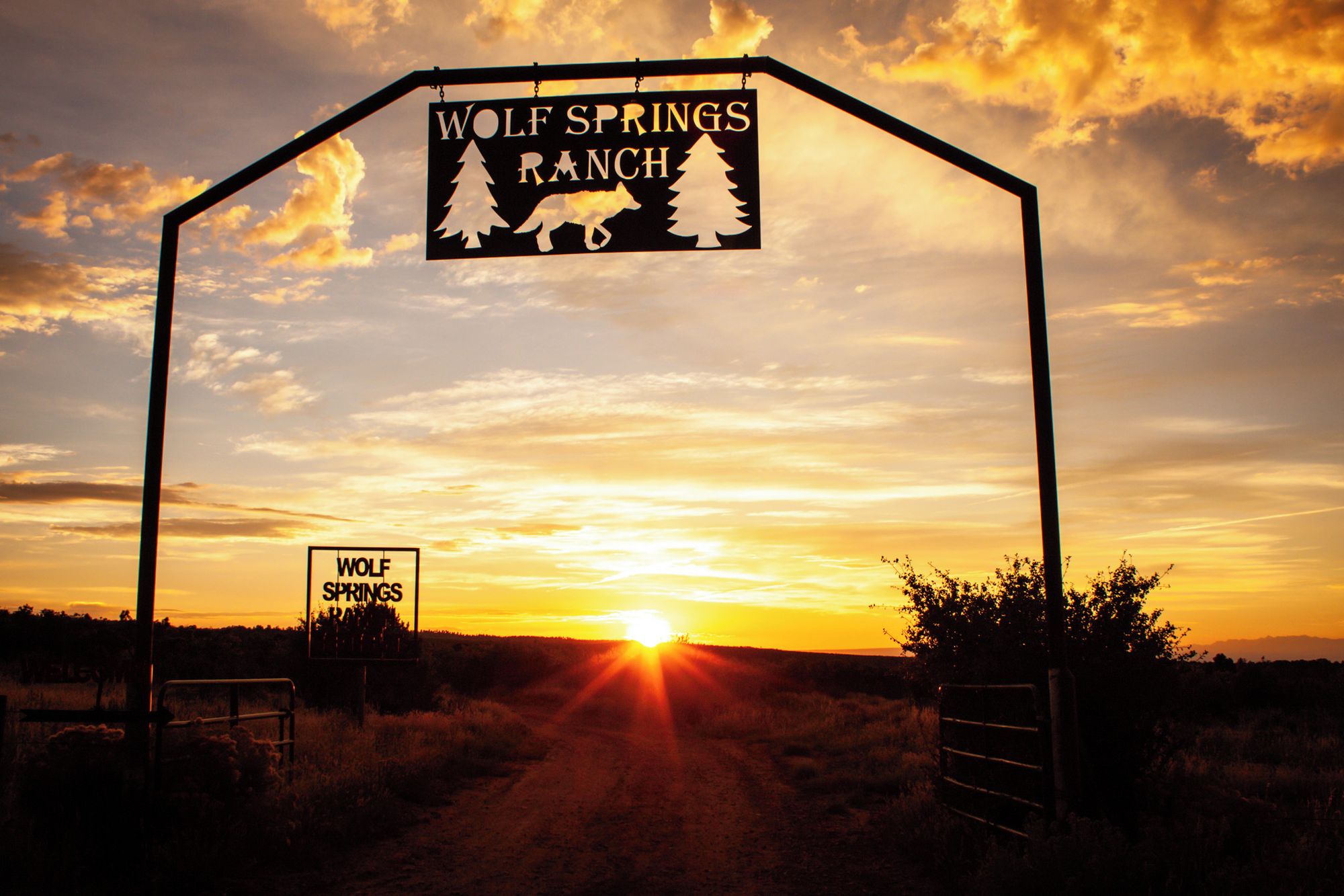 A sign for Wolf Springs Ranch with a sunset in the background.