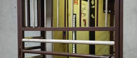 Una ventana con rejas de metal, un panel de control de ascensor visible y una pared con un cartel.