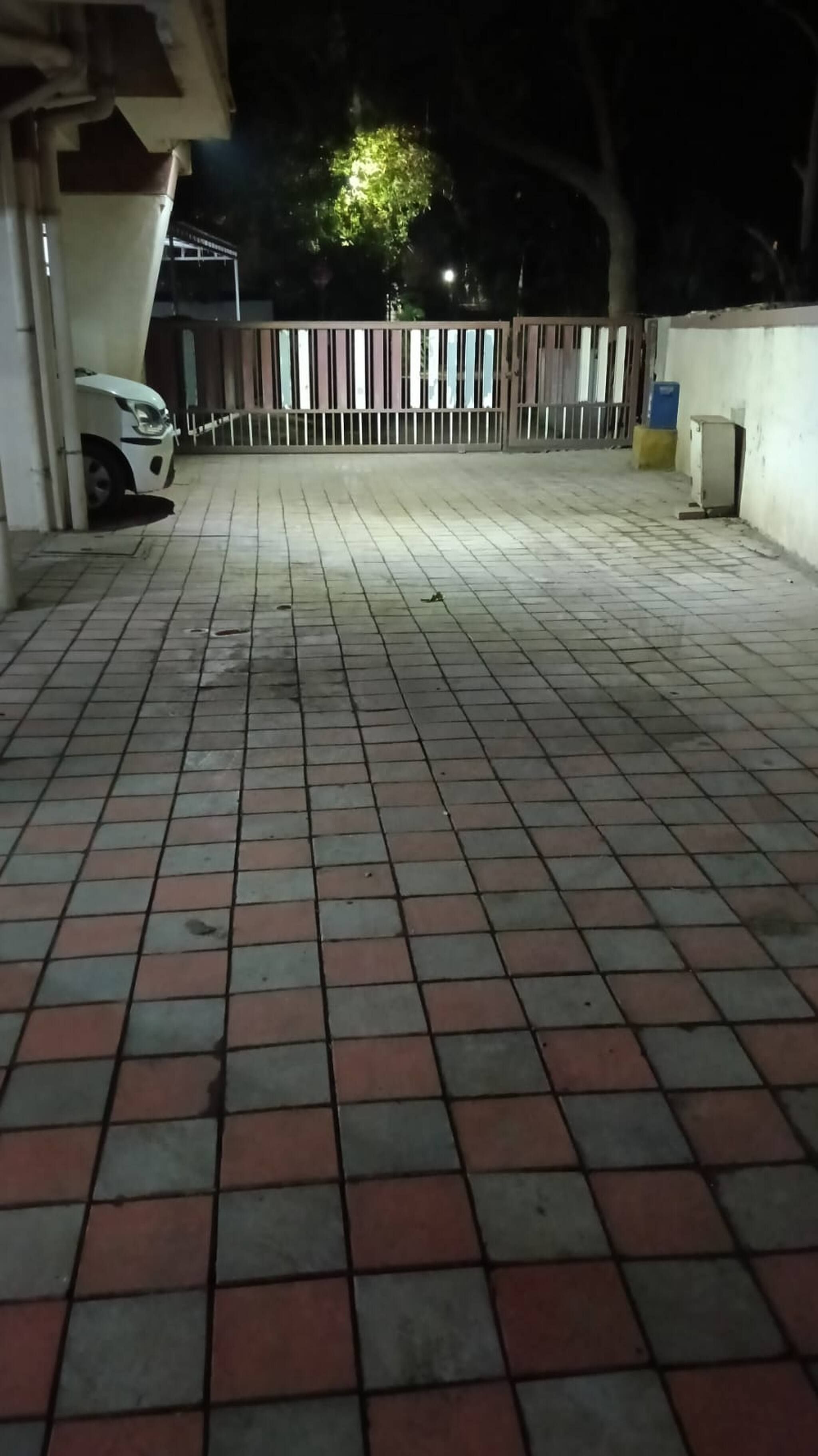 A paved outdoor area with a car parked on the left and a fence in the background.
