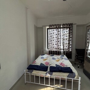 A bedroom with a single bed, a chair, a desk, and a window with curtains. - Comfortable 3 BHK Homestay (Nashik)
