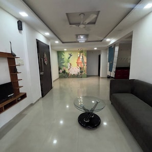 A modern living room with a glass coffee table, a sofa, a mural, and a ceiling fan. - Comfortable 3 BHK Homestay (Nashik)