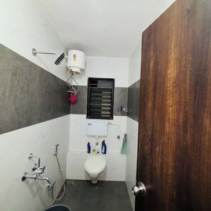 A small bathroom with a toilet, a shower, a hand dryer, and a window. - Comfortable 3 BHK Homestay (Nashik)