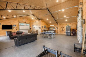 A spacious indoor area with a ping pong table, seating, and a garage door. - Nolin Lake | Sleeps 10 | Private | Community Pool (Clarkson)