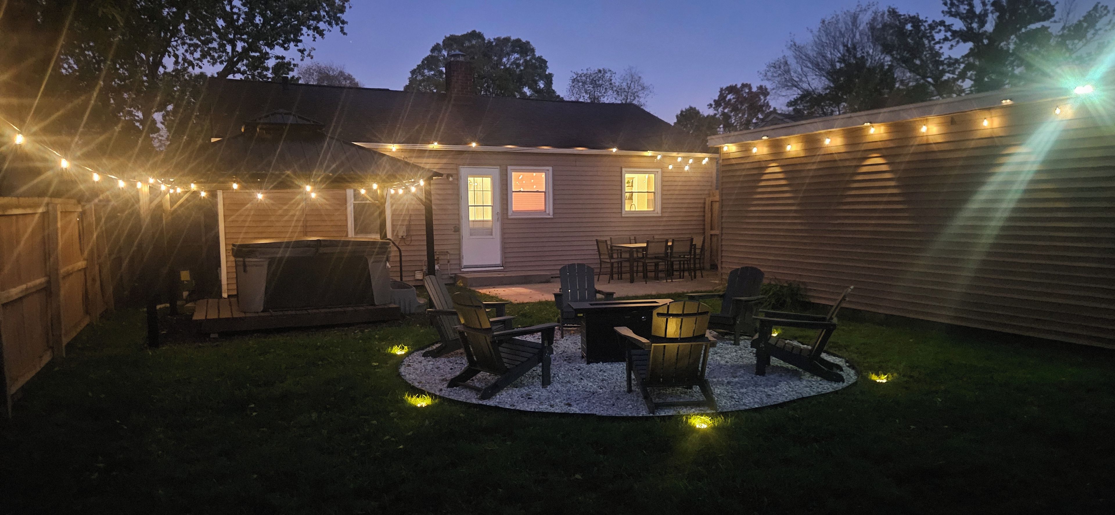 Un jardin avec une terrasse, du mobilier d’extérieur et des guirlandes lumineuses.