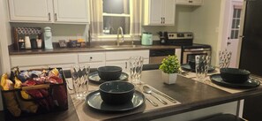 A kitchen with a dining table set for two, featuring black plates, clear glasses, and a small potted plant. - Notre Dame Retreat I Hot Tub, Fire Pit & EV Charger (South Bend)