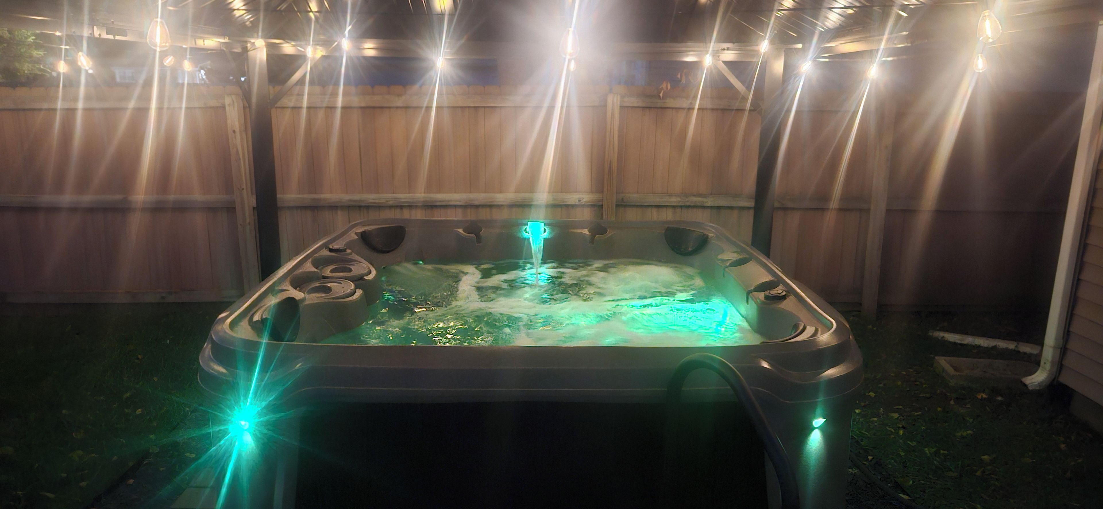 A hot tub with a built-in heater, surrounded by a wooden fence, and illuminated by string lights.