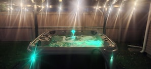 Una vasca idromassaggio con riscaldatore integrato, circondata da una recinzione in legno e illuminata da luci a stringa.