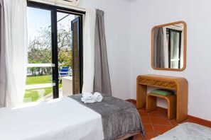A hotel room with a bed, a small desk with a chair, a mirror, and a view of the outdoors. - New Listing (Albufeira)