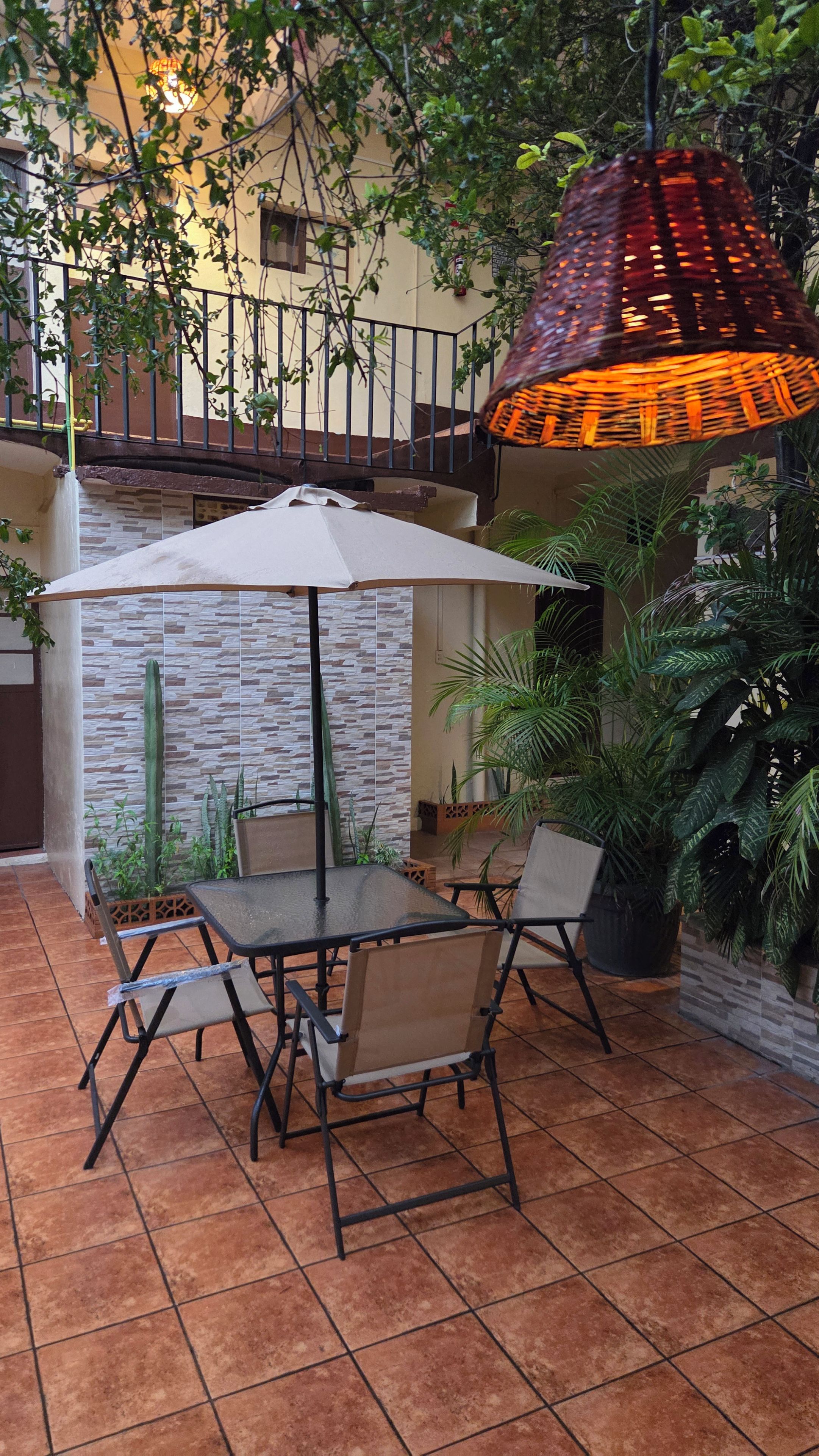 Eine Terrassengruppe mit Tisch und Stühlen, umgeben von Pflanzen und einer Hängelampe.