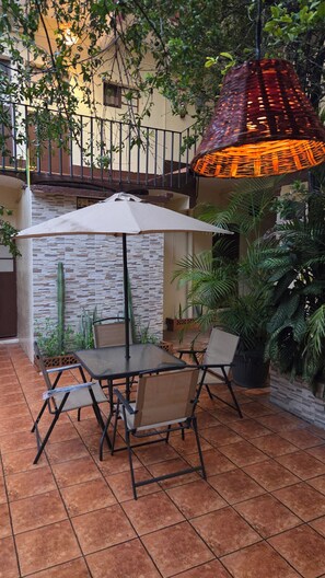 Eine Terrassengruppe mit Tisch und Stühlen, umgeben von Pflanzen und einer Hängelampe.