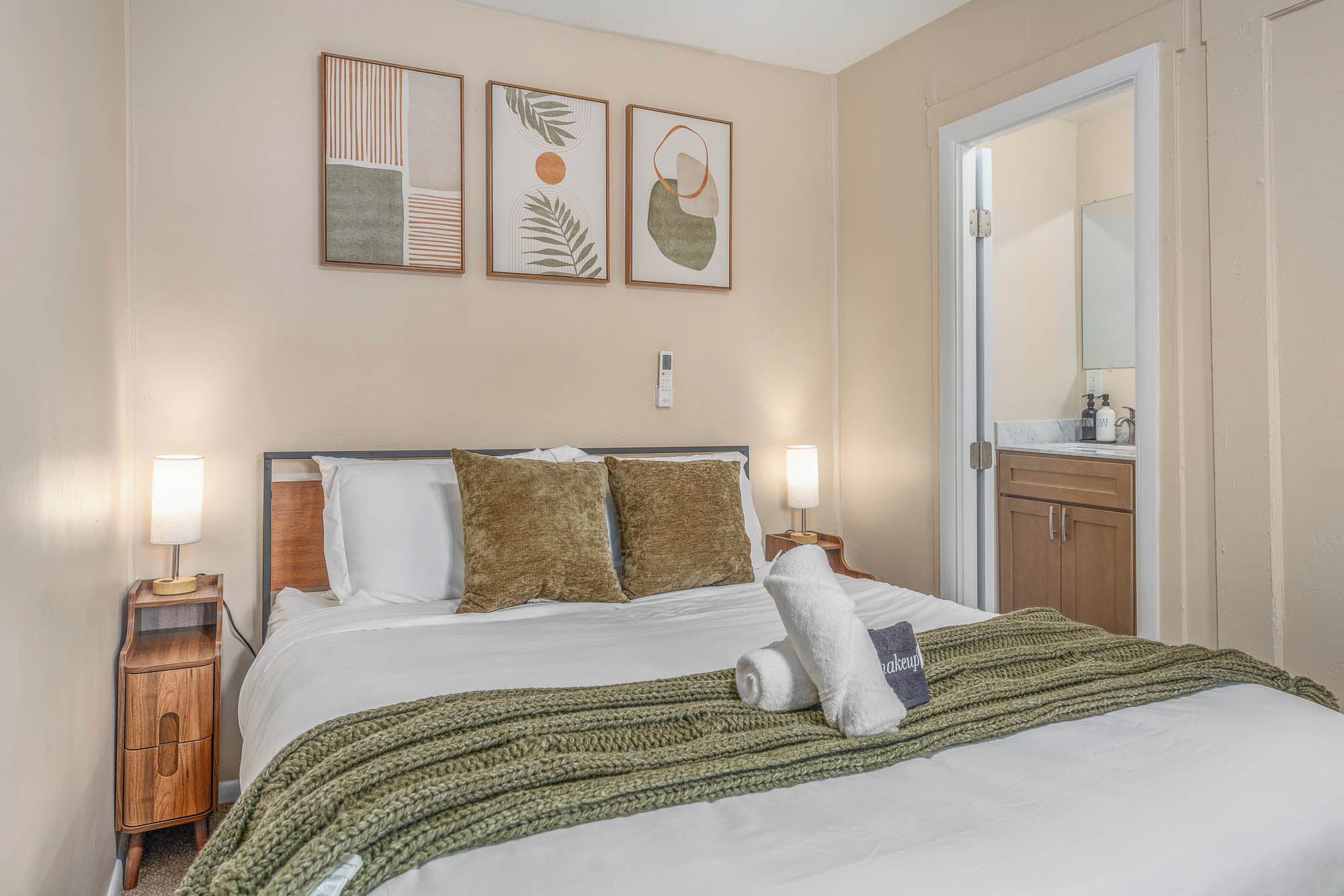 Een hotelkamer met een bed, een nachtkastje, een badkamer met een spiegel en wanddecoratie.