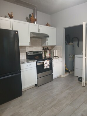 A kitchen with white cabinets, a black refrigerator, a stove, and a microwave. - Historic and Charming in the Heart of Town (Fort Worth)