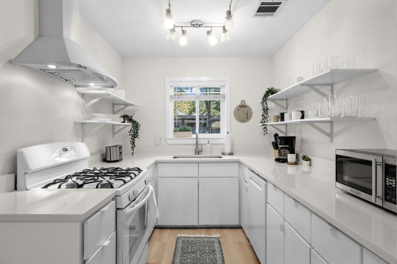 A modern kitchen with white cabinetry, a gas stove, a microwave, and a window with a view of greenery.