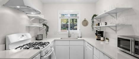A modern kitchen with white cabinetry, a gas stove, a microwave, and a window with a view of greenery.