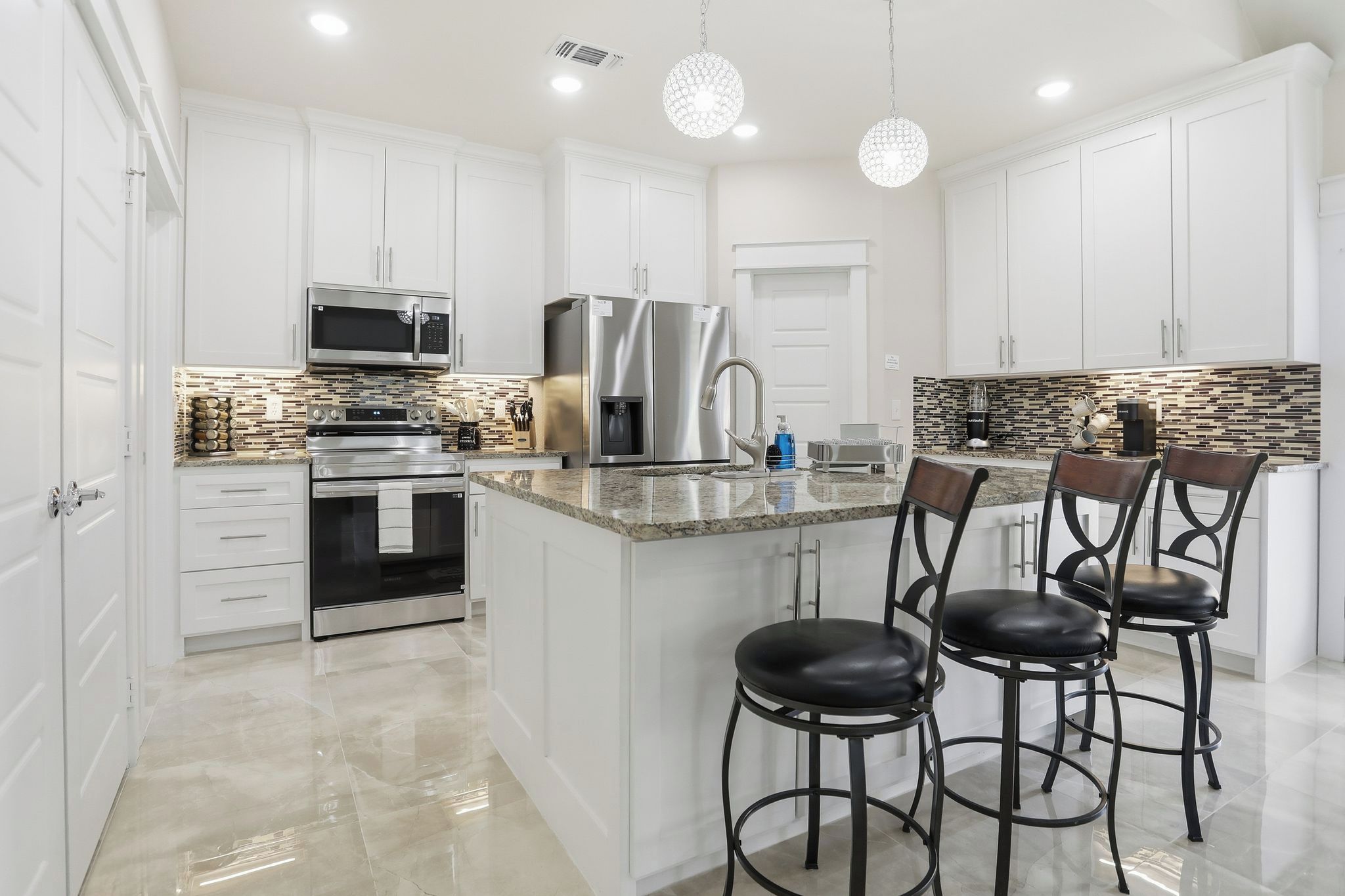 A modern kitchen with white cabinetry, stainless steel appliances, a granite countertop, and a bar area with stools.