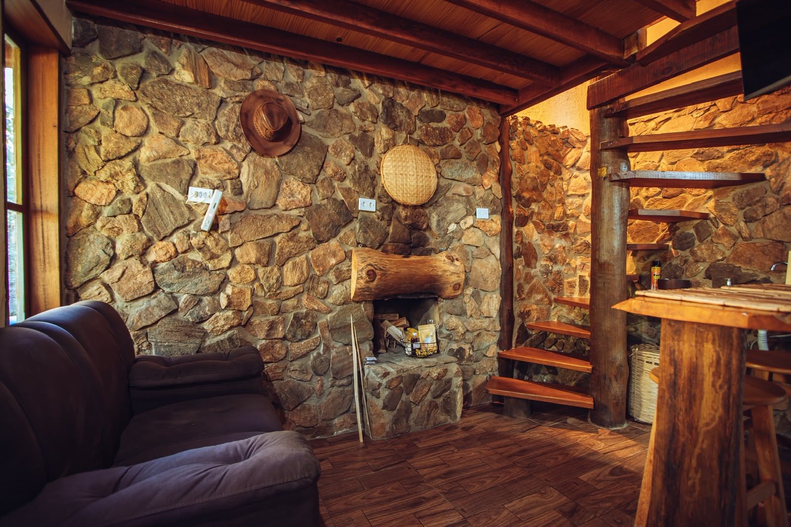 A rustic interior with a stone wall, a fireplace, a wooden bench, and a leather sofa.