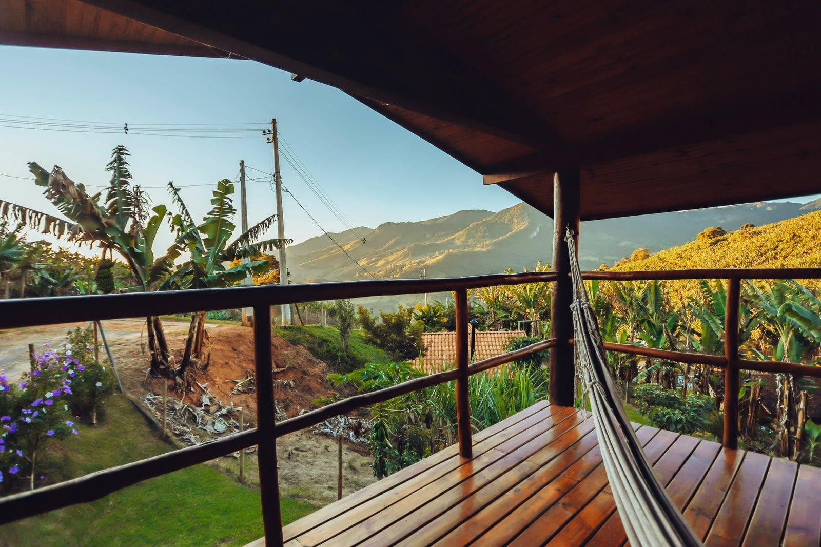 Une terrasse en bois offrant une vue sur un paysage montagneux, avec des bananiers et un ciel dégagé.