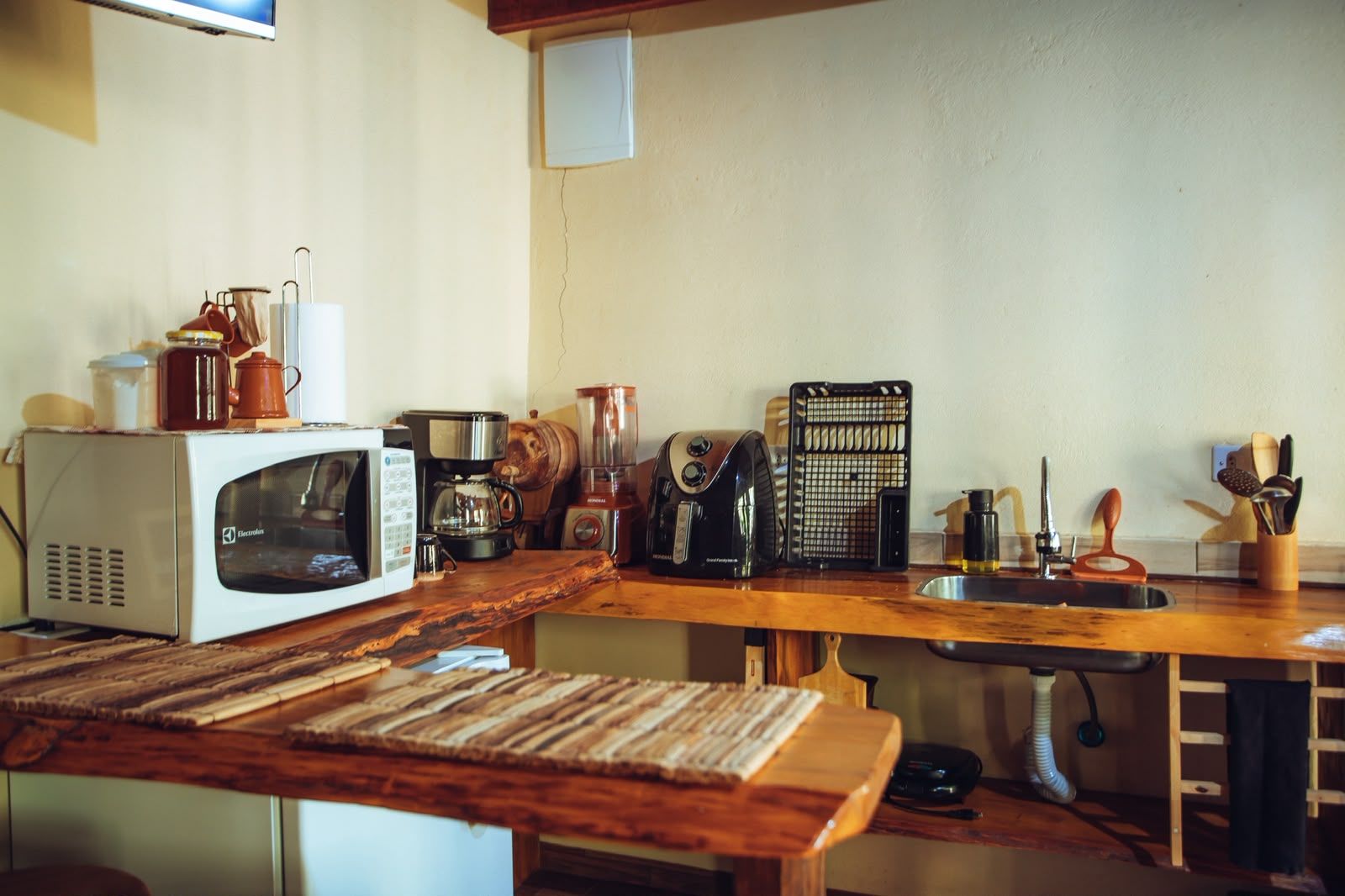 Una cocina con cubierta de madera, microondas, cafetera, licuadora y diversos utensilios de cocina.