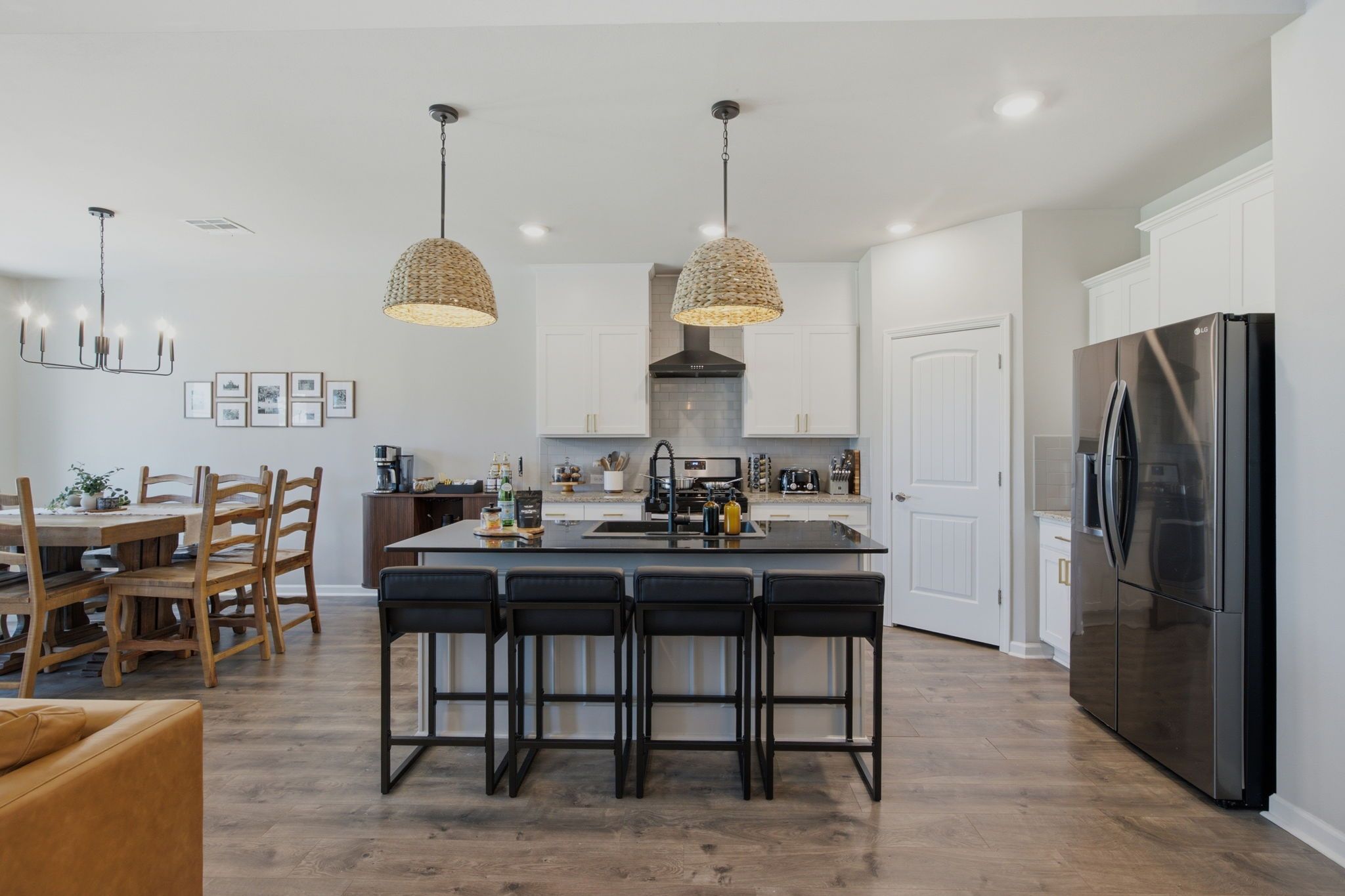 A modern kitchen with a central island, bar stools, a stainless steel refrigerator, and pendant lighting.