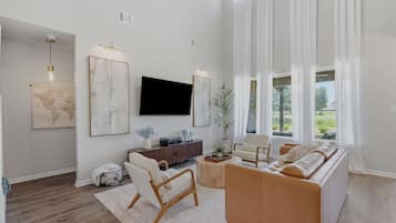 Uma sala de estar ampla com um sofá grande, uma mesa de centro e uma TV de tela plana na parede.