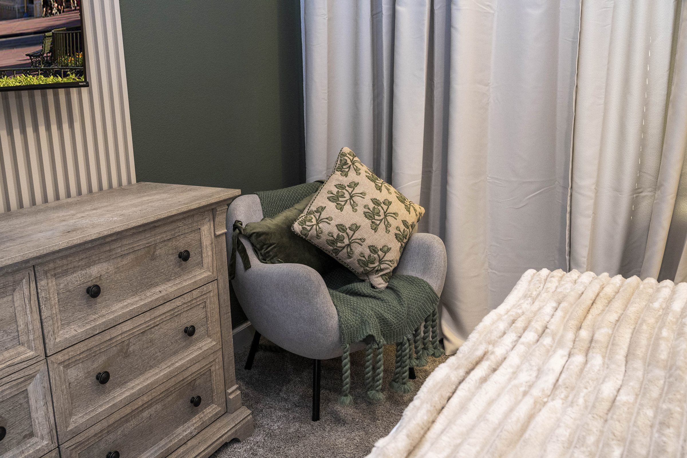 Een kamer met een houten dressoir, een grijze fauteuil, een kussen met een patroon en een witte deken.
