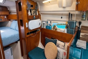 Un interior compacto con una cama litera, una pequeña zona de estar con cojines, un espejo y vista al mar.
