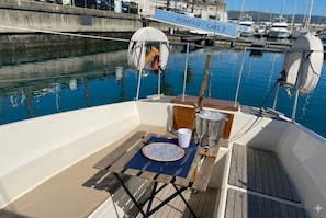 Cubierta de barco con una mesa para dos, un balde metálico y un letrero que dice 'PONTÃO - CAIS 2'.