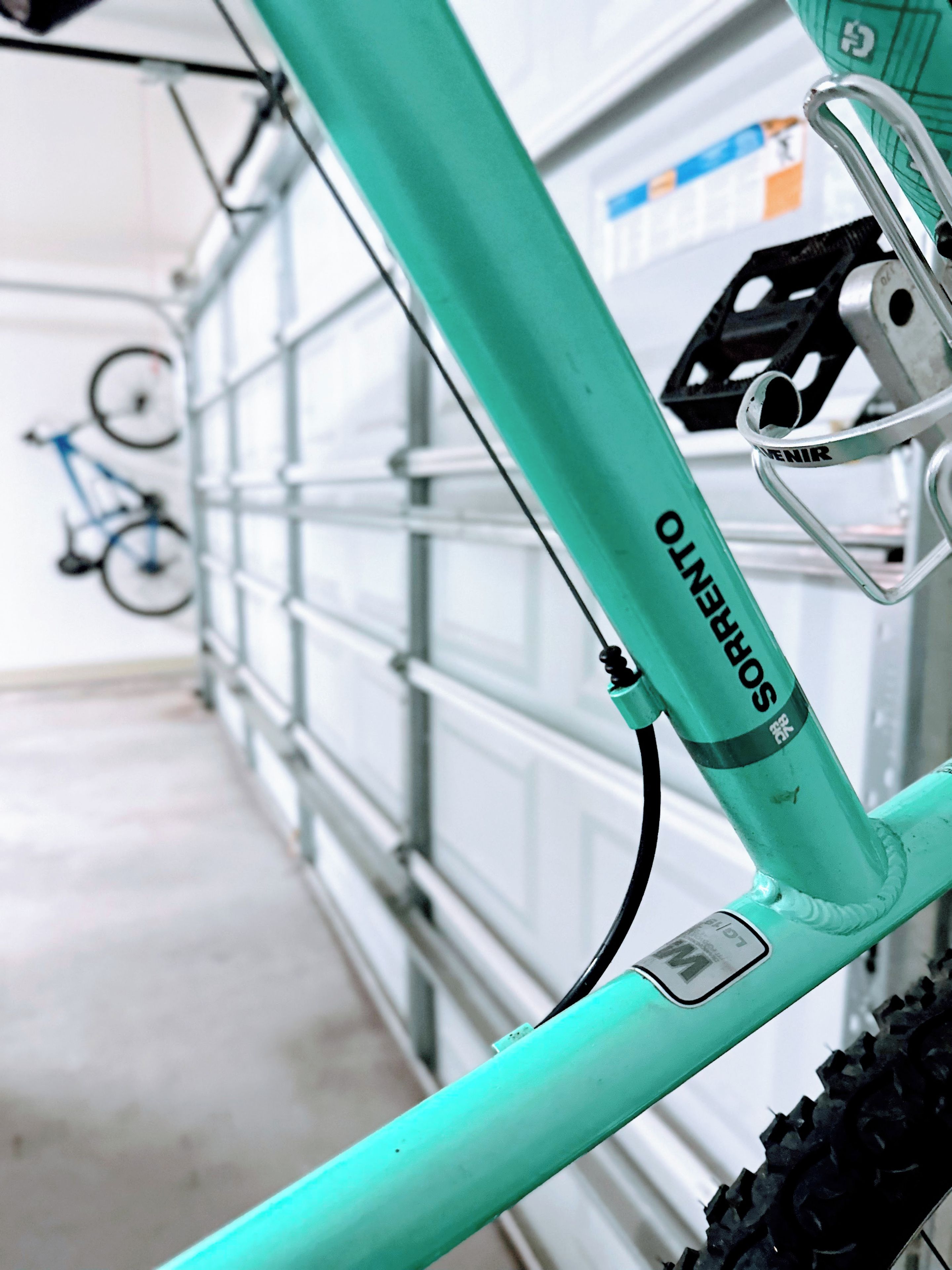 A bicycle with a green frame and a black seat, parked indoors with a garage door in the background.