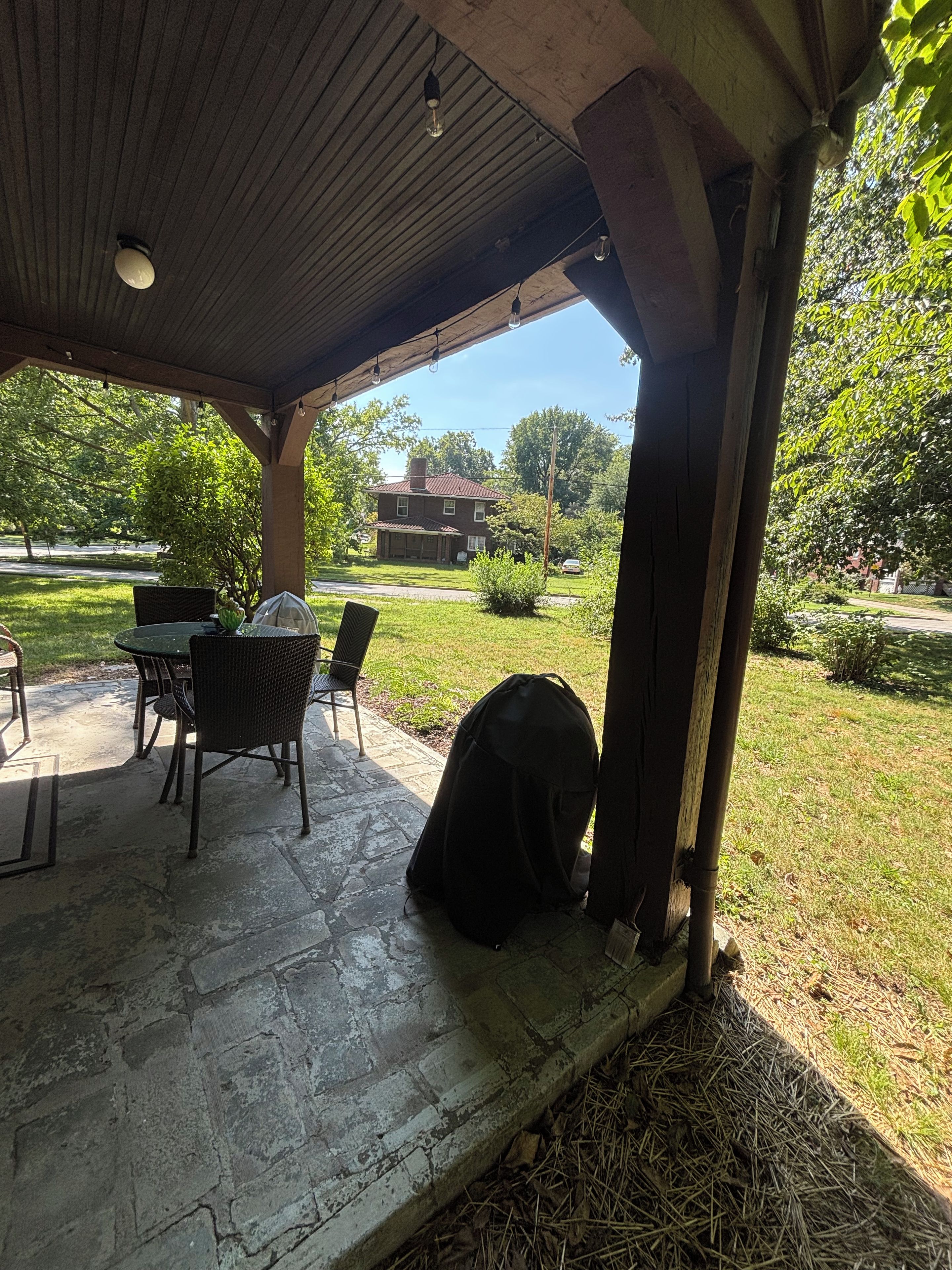 A covered patio with a table and chairs, a grill, and a bag on the ground.