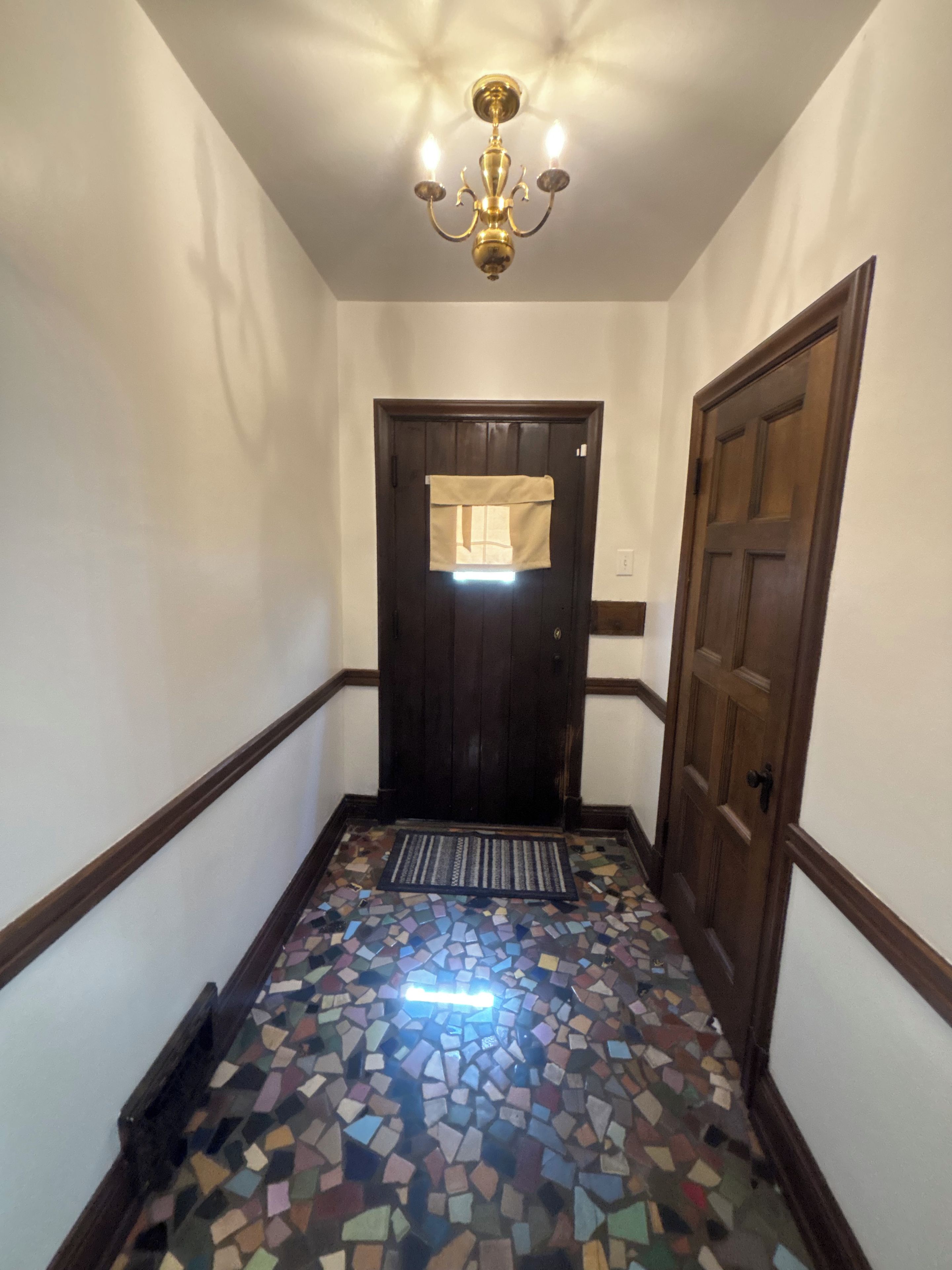Un pasillo con suelo de mosaico, una puerta de madera oscura y un candelabro.