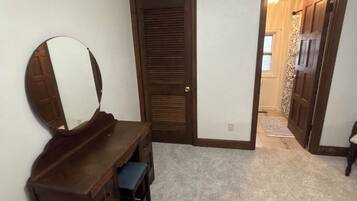 A bedroom with a wooden dresser, a mirror, a bed, and a door leading to another room.