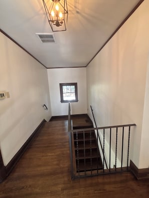 Una escalera de madera con barandilla de metal que lleva a un rellano con un pequeño ventanal.