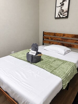 A single bed with a wooden headboard, a green quilt, and a gray bag with a sign on it. - Spacious 3BR Jacksonville Home—Sleeps Up to 8 (Jacksonville)