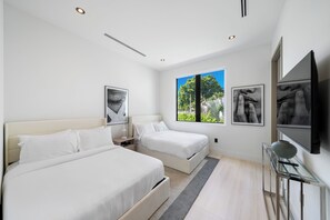 Ein modernes Schlafzimmer mit zwei Betten, einem großen Fenster und Bildern an den Wänden.